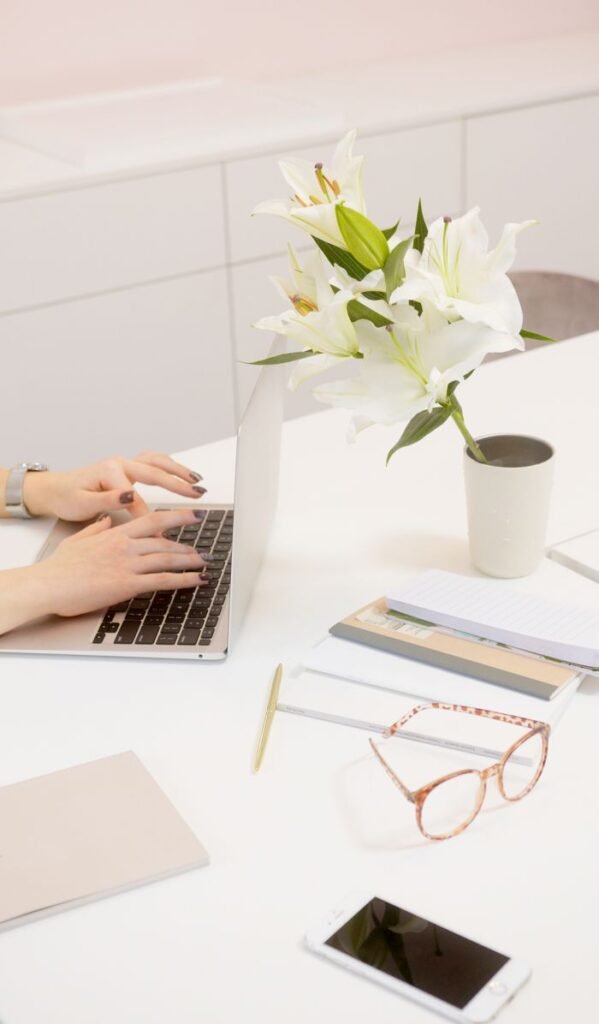 A serene workspace featuring a laptop, flowers, and office supplies on a white desk.