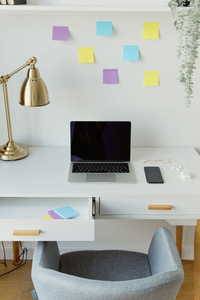 A minimalist home office desk setup with a laptop, phone, and gold lamp.